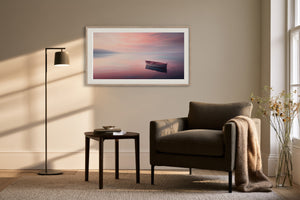 White-framed rowboat artwork above an armchair, side table, and floor lamp.