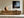 Framed misty pine shoreline artwork above a wood sideboard with ceramic vessels.