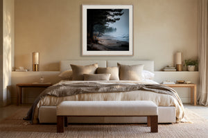 Framed misty coastal artwork centered above a bed with neutral bedding.
