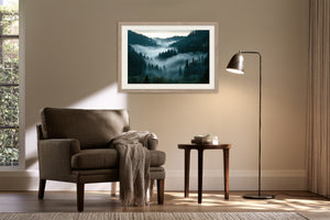 Light wood-framed misty forest artwork above an armchair beside a floor lamp and side table.
