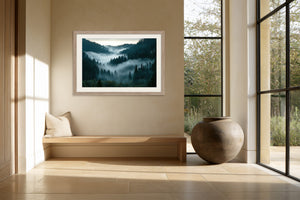 Light wood-framed misty forest artwork above a built-in bench beside large black-framed windows.