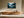 Light wood-framed misty conifer forest artwork above a long wooden sideboard in a sunlit space.