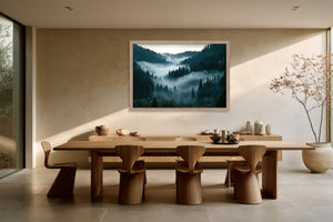 Light wood-framed misty forest artwork above a long wooden dining table with sculptural chairs.