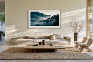 Framed misty conifer forest artwork above a cream sofa in a sunlit living area.