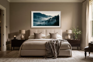 Framed forest landscape centered above a bed with neutral bedding and dark bedside tables.