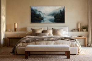 Framed misty conifer lake artwork centered above a bed with neutral bedding.