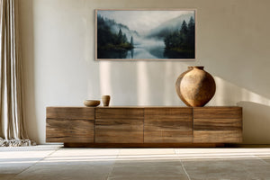 Framed misty forest lake artwork above a wooden sideboard with ceramic vessels.