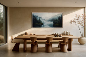 Framed misty forest lake artwork above a long wooden dining table and sculptural chairs.