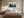 Light wood-framed misty pine forest artwork above a bed with cream bedding and matching bedside lamps.