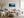 Light wood-framed misty pine forest artwork above a cream sofa and wood coffee table.