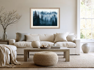Light wood-framed misty pine forest artwork above a cream sofa and wood coffee table.