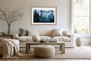 Light wood-framed misty pine forest artwork above a cream sofa and wood coffee table.