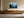 Light wood-framed misty pine forest artwork displayed above a long wooden sideboard with ceramic vessels.