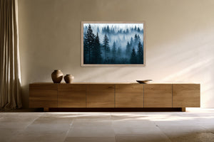 Light wood-framed misty pine forest artwork displayed above a long wooden sideboard with ceramic vessels.
