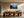 Light wood-framed misty pine forest artwork above a large wooden dining table with sculptural chairs.