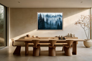 Light wood-framed misty pine forest artwork above a large wooden dining table with sculptural chairs.
