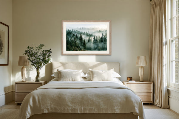 Light wood-framed misty evergreen forest artwork above a white bed between two bedside tables.