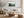Light wood-framed misty forest artwork above a white sofa, with a wood coffee table and woven ottoman.