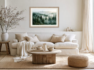 Light wood-framed misty forest artwork above a white sofa, with a wood coffee table and woven ottoman.