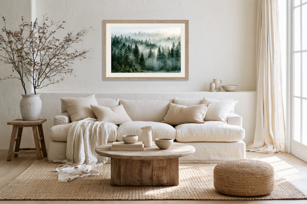 Light wood-framed misty forest artwork above a white sofa, with a wood coffee table and woven ottoman.