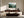 Light wood-framed evergreen forest artwork above a dark wood sideboard behind a curved white sofa.