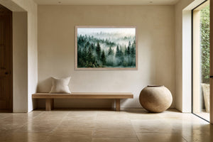 Light wood-framed misty forest artwork above a low wooden bench beside a large ceramic vessel.