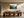 Light wood-framed misty evergreen forest artwork above a long wooden dining table with sculptural chairs.
