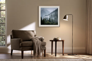 Framed misty mountain forest artwork above a brown armchair beside a floor lamp and side table.