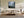 Misty mountain forest artwork in a slim wood frame above a low cream sofa and coffee table.