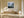 White-framed misty mountain forest artwork above a wooden bench beside a large ceramic vase.