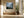 Framed misty mountain forest artwork above a built-in bench beside tall black-framed windows and a large urn.
