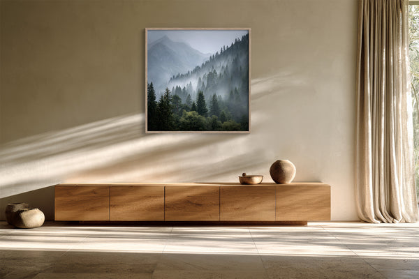 Misty mountain forest artwork in a slim wood frame above a long wooden sideboard.