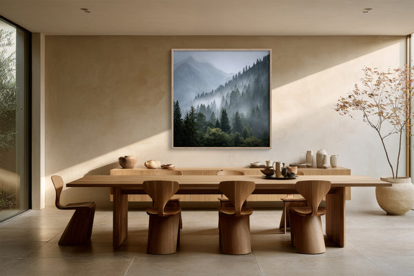 Framed misty mountain forest artwork above a long wooden dining table with sculptural chairs.