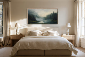Mist Between the Pines mountain river artwork in a light wood frame above a bed between matching lamps.