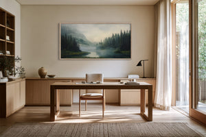 Light wood-framed misty river landscape above a wooden desk in a bright workspace.