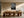 Framed raindrop-covered leaf photograph above a long wooden dining table with sculptural chairs.