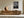 Framed monochrome leaf photograph above a low wooden sideboard with ceramic vase and bowls.