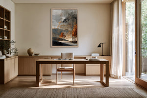 Light wood-framed autumn trees print displayed above a wooden desk in a sunlit office.