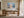 Light wood-framed mountain lake artwork above a wooden desk beside tall windows.