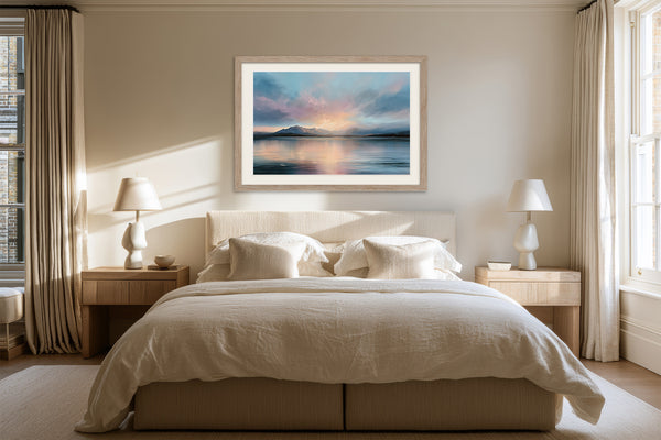 Light wood-framed mountain lake artwork centered above a bed with cream linens.