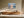 Light wood-framed mountain lake artwork above a low wooden sideboard in sunlit space.