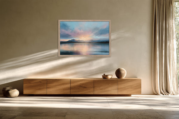 Light wood-framed mountain lake artwork above a low wooden sideboard in sunlit space.