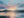 Painterly mountain range beneath pink and blue clouds reflected across a calm lake.