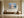 Light wood-framed mountain lake artwork above a bench beside a large ceramic vessel.