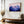 Violet Ranges mountain artwork in a gold-toned frame above a wooden bench and vase.