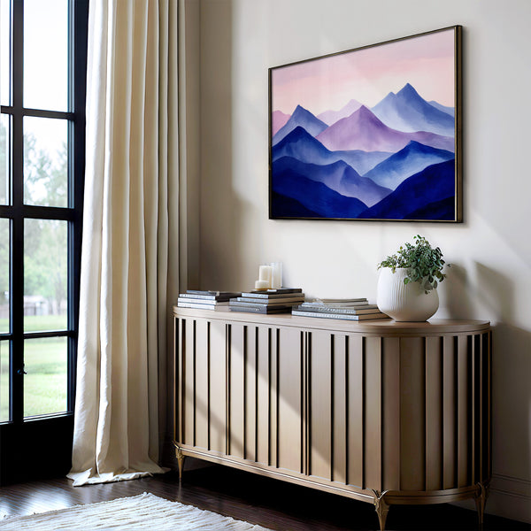 Violet Ranges mountain artwork in a dark slim frame above a console with books and a plant.