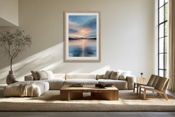 Light wood-framed mountain lake artwork above a cream sectional sofa in a sunlit living area.