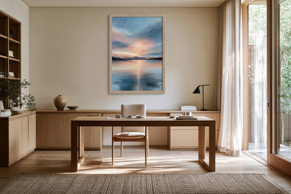 Light wood-framed mountain lake artwork displayed above a wooden desk beside tall glass doors.