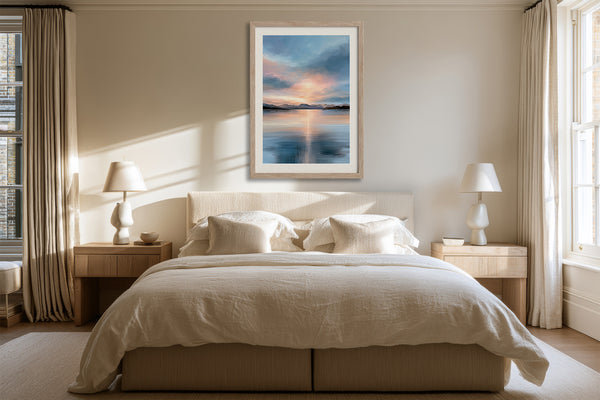 Light wood-framed mountain lake artwork above a neatly made bed between matching bedside lamps.
