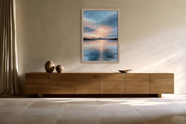 Light wood-framed mountain lake artwork hanging above a long wooden sideboard with ceramic vessels.